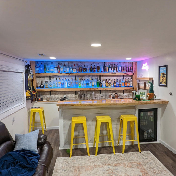 Spacious home bar with wooden flooring, yellow stools, illuminated shelves stocked with various liquor bottles. Spacious home bar with wooden flooring, yellow stools, illuminated shelves stocked with various liquor bottles.