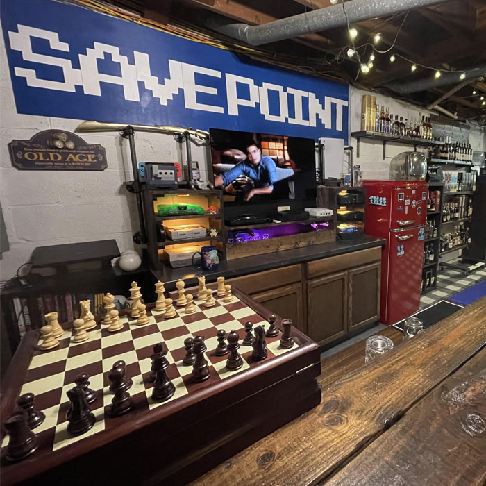 Home bar setup with game consoles, a chessboard, vintage fridge, and liquor shelves for a fun happy hour experience. Home bar setup with game consoles, a chessboard, vintage fridge, and liquor shelves for a fun happy hour experience.