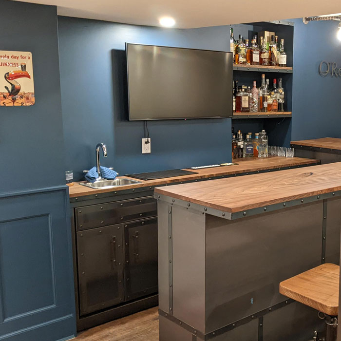 Small blue home bar with a sink, wooden countertop, metal accents, and shelves stocked with liquor bottles for happy hour ideas. Small blue home bar with a sink, wooden countertop, metal accents, and shelves stocked with liquor bottles for happy hour ideas.