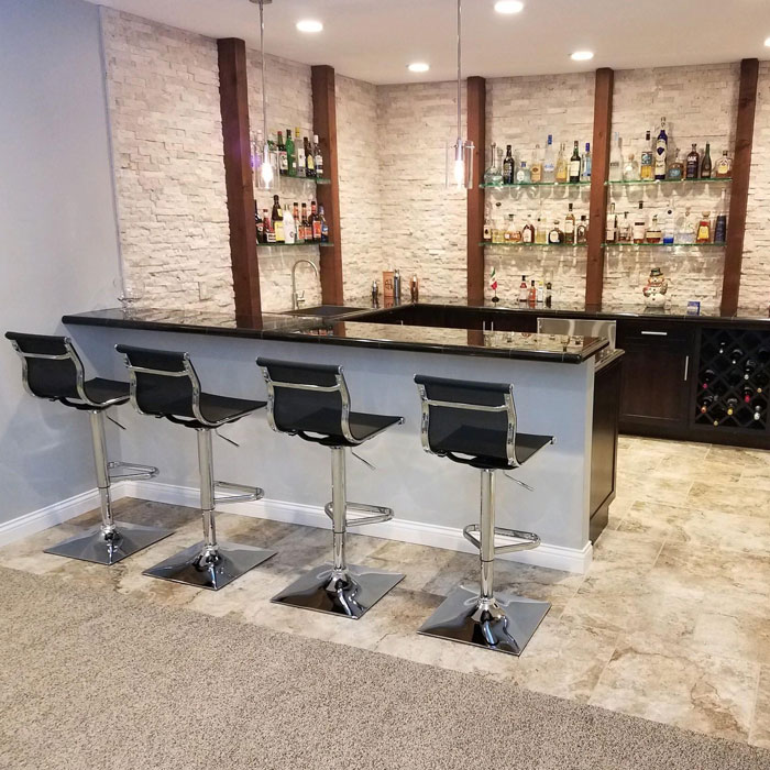 Modern black and white home bar setup with high stools, stone wall, and shelves stocked with various liquor bottles. Modern black and white home bar setup with high stools, stone wall, and shelves stocked with various liquor bottles.