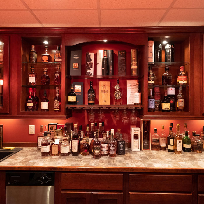 Poorly lit brown home bar with various liquor bottles and glassware, showcasing cozy home bar ideas for happy hour. Poorly lit brown home bar with various liquor bottles and glassware, showcasing cozy home bar ideas for happy hour.