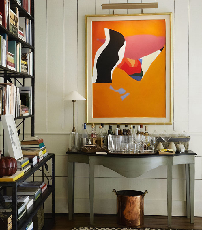 Abstract wall art above a small home bar setup with bottles and glassware for happy hour entertaining. Abstract wall art above a small home bar setup with bottles and glassware for happy hour entertaining.