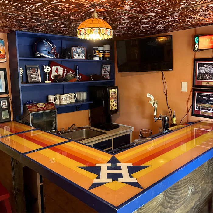 Colorful sports-themed home bar featuring Houston Astros logo, memorabilia, and vibrant striped countertop for happy hour enjoyment. Colorful sports-themed home bar featuring Houston Astros logo, memorabilia, and vibrant striped countertop for happy hour enjoyment.