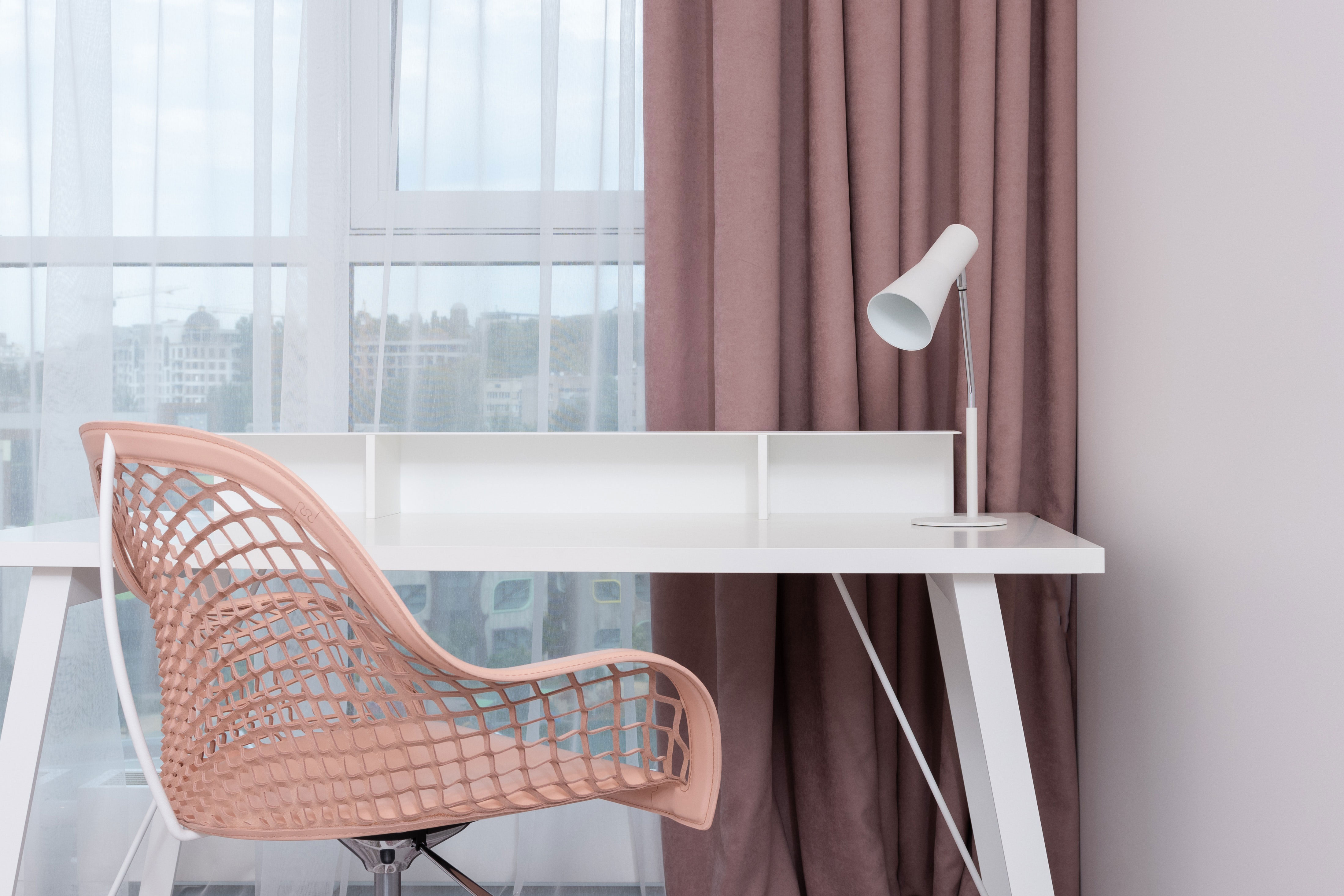 Home office ideas with pink curtains and chair near a white table and modern desk lamp for productive work.