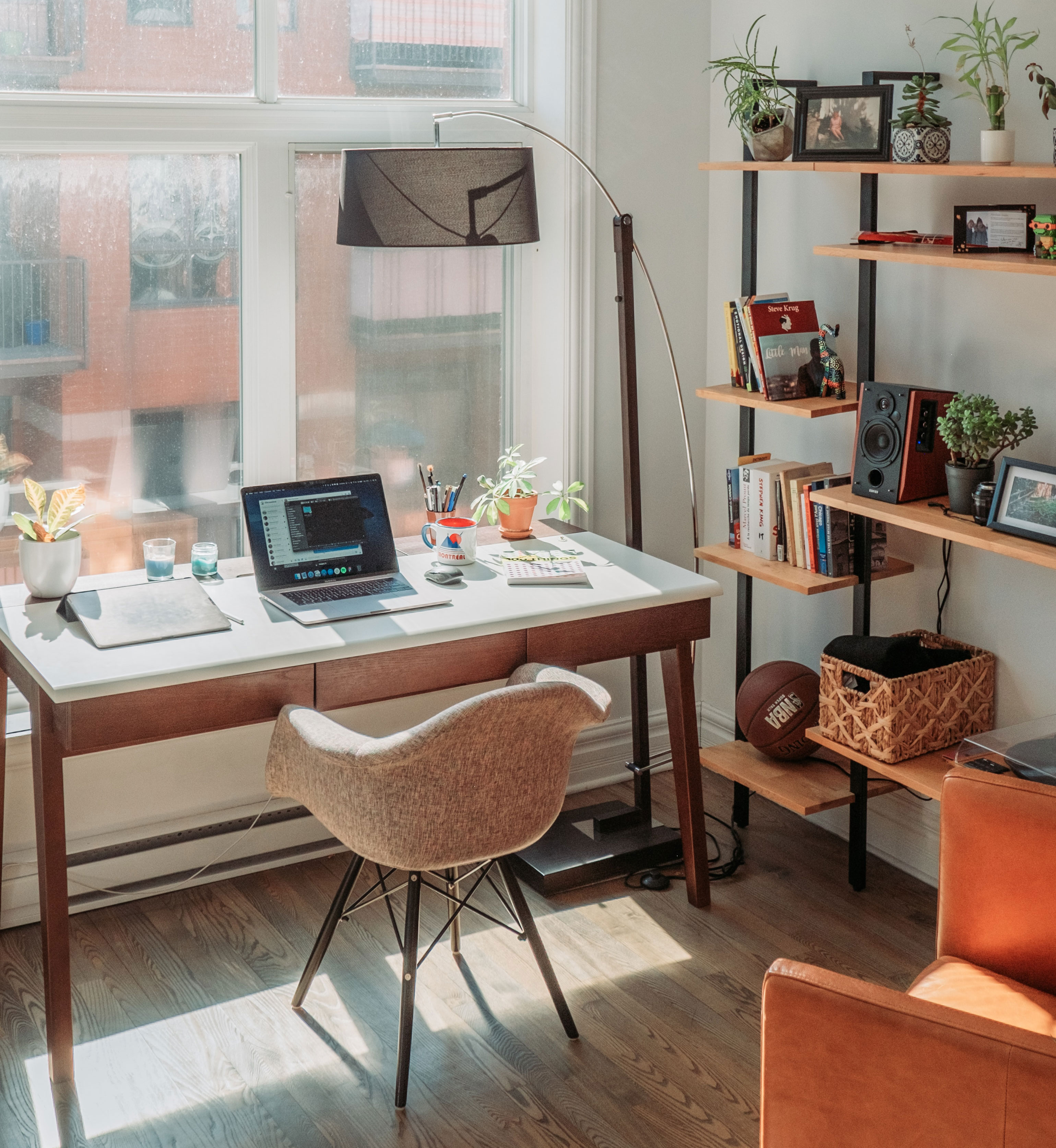 Bright home office with black laptop on wooden table, modern chair, plants, and shelves for an inspired and productive work process