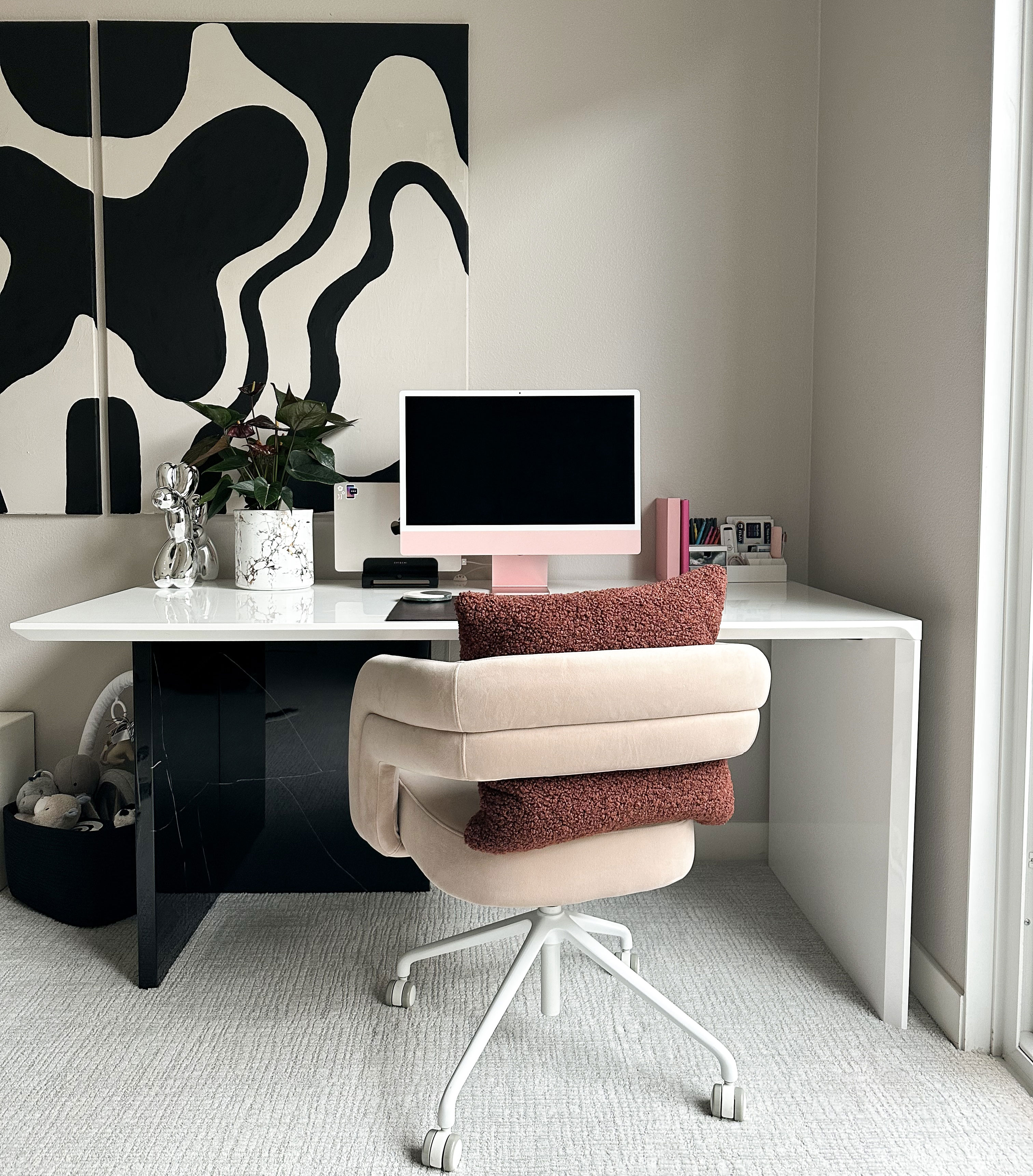 Minimalist home office setup with large-scale abstract art, pink computer, and comfortable swivel chair for productivity.