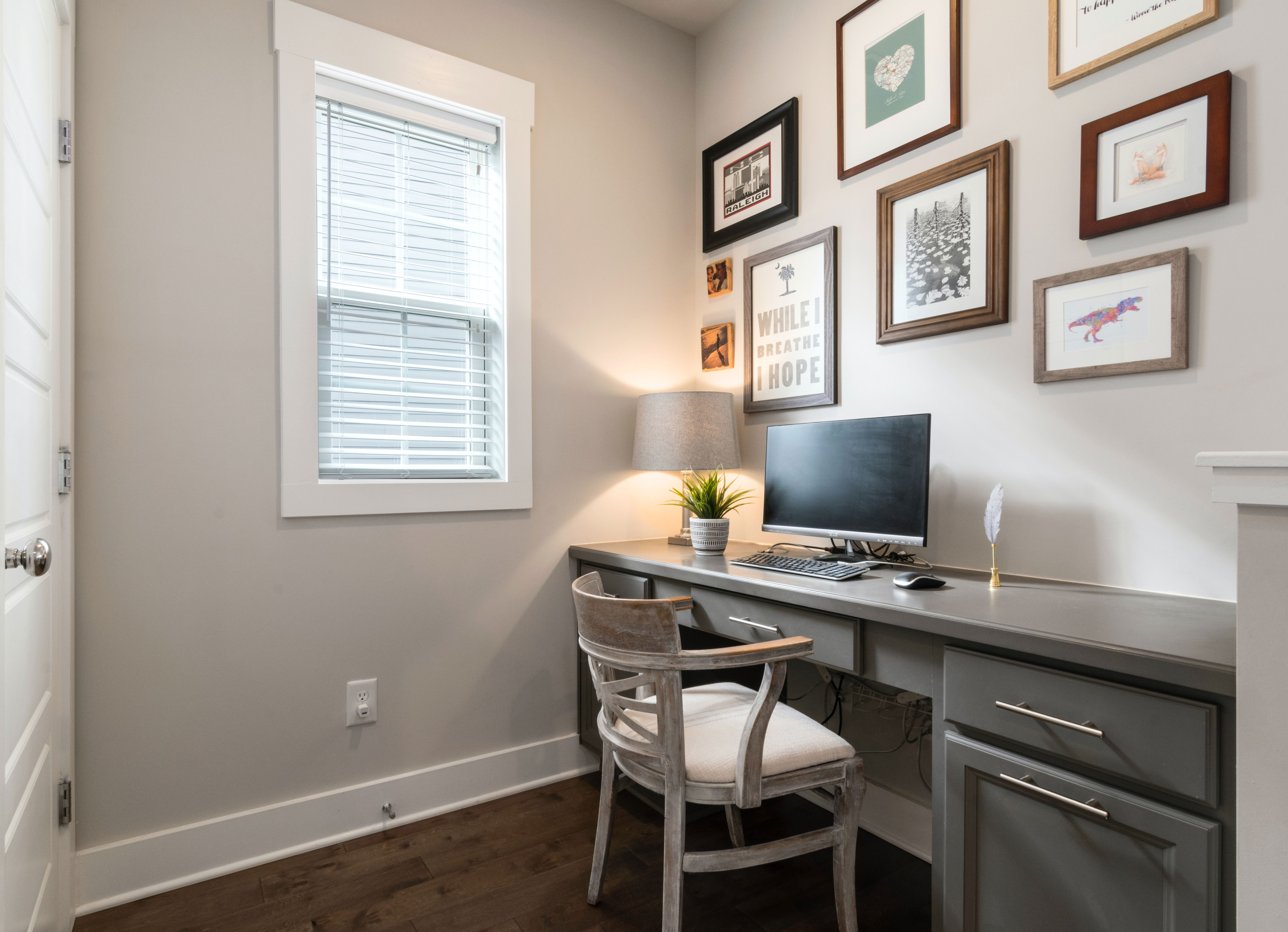 Home office ideas featuring framed pictures on wall above a desk with computer, chair, and desk lamp for productivity.