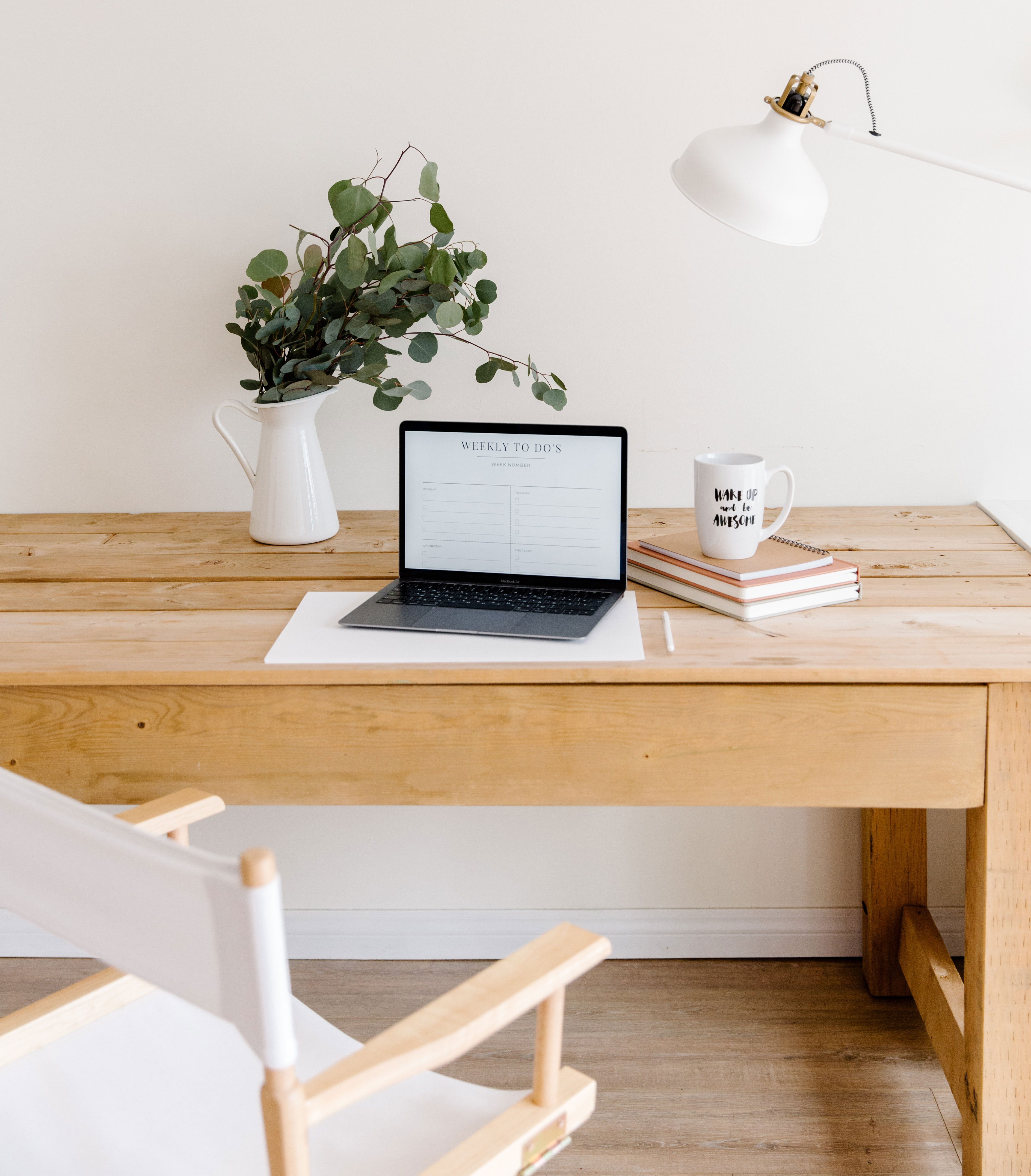 Minimalist home office setup with wooden desk, laptop, plant in vase, white chair, and task lamp for productive workspace ideas