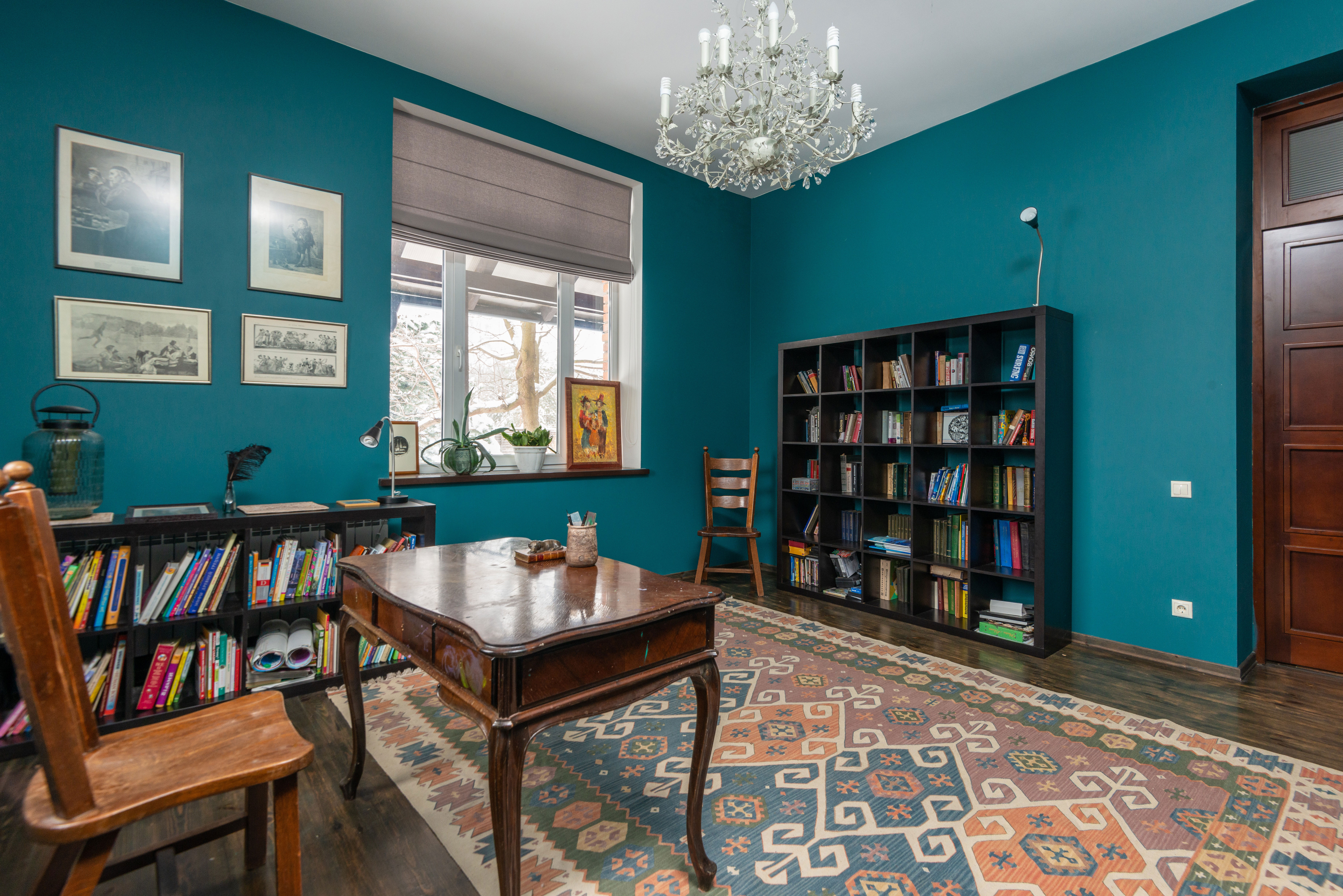 Home office ideas featuring a room with bookshelves, a wooden table, chairs, and teal walls for productivity.