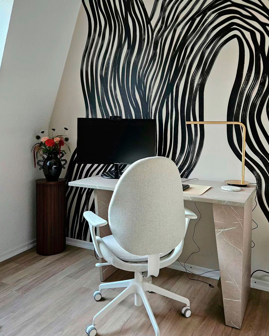 Home office setup featuring a monitor opposite a black and white accent wall with a modern chair and desk.
