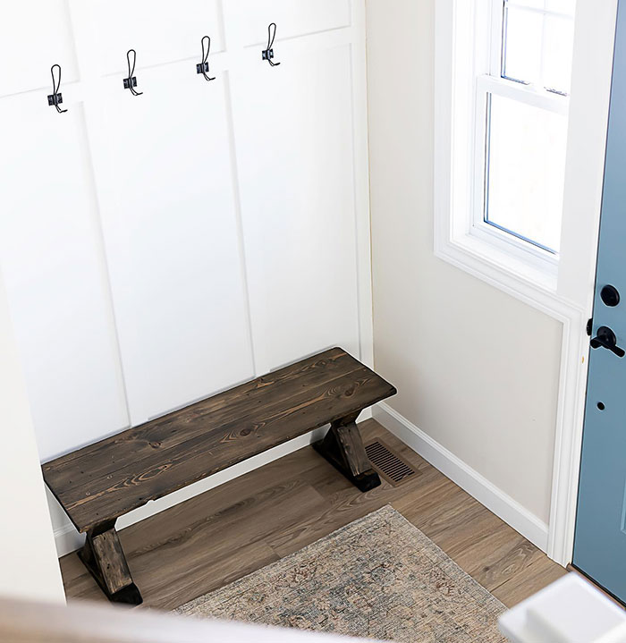 Ebony wood stain on a bench in a bright anteroom with white walls, hooks, and natural light from a window.