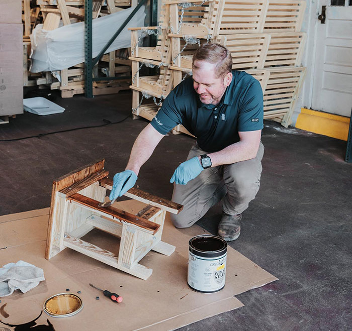Man applying wood stain to a chair, demonstrating Minwax stain colors for choosing wood stain color in a workshop setting.