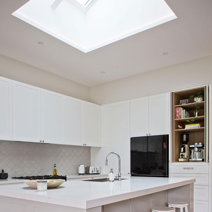 Spacious bright modern kitchen design featuring white cabinets, a skylight, and a large central island with seating.