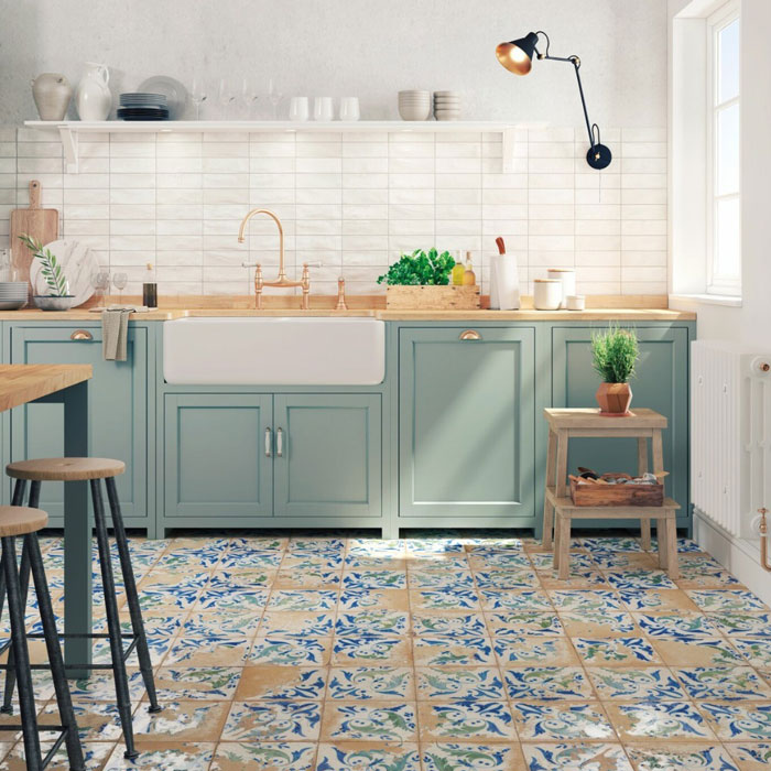 Modern kitchen design featuring colorful statement floor tiles, pastel green cabinets, and a farmhouse sink with natural light.