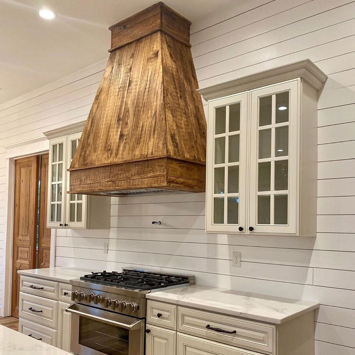 Statement piece hood in a bright kitchen featuring modern kitchen designs for a timeless look with white cabinetry and marble countertops