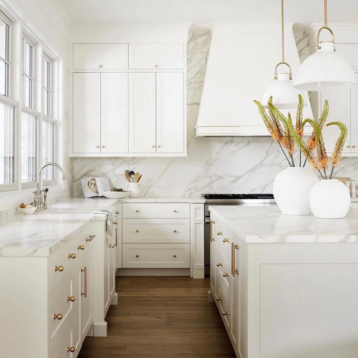 Bright white kitchen featuring modern kitchen design with marble countertops and brass hardware accents.