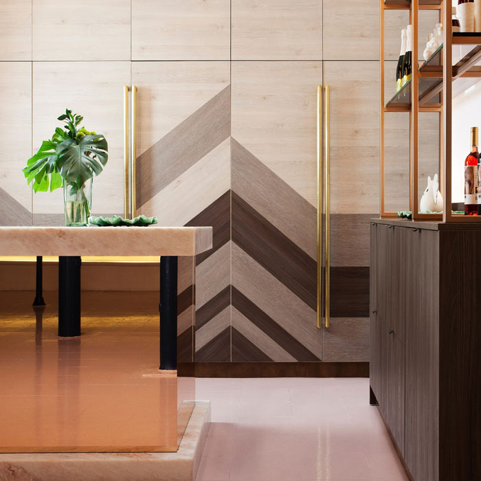 Brownish modern kitchen design featuring chevron wood cabinets, gold handles, wall art, and a minimalist dining table with greenery.