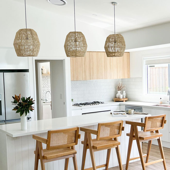 Spacious bright kitchen featuring modern kitchen designs with wooden chairs and natural pendant lights above the island.