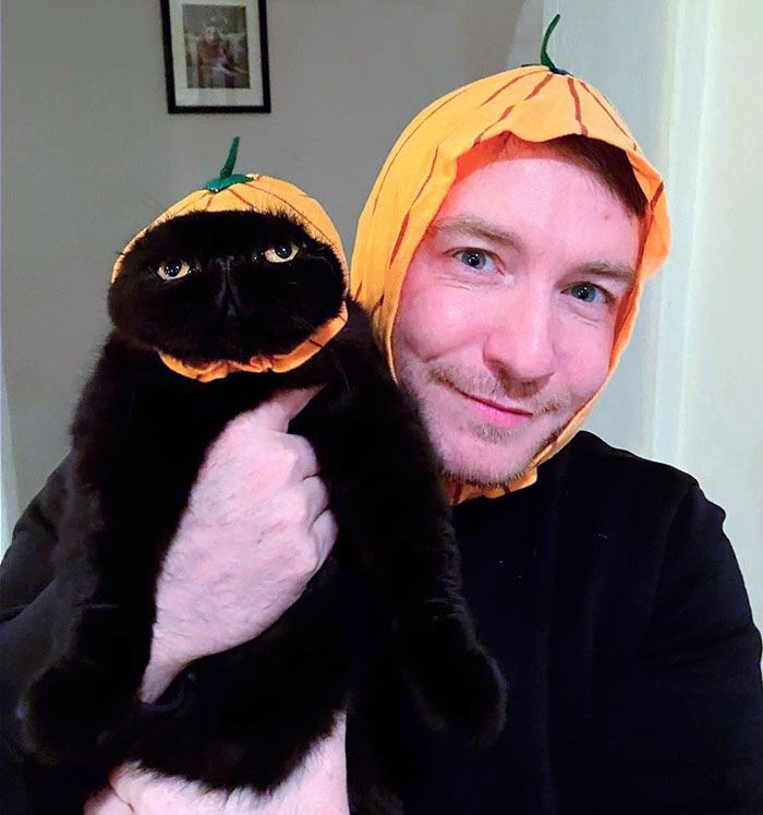 Man and black cat wearing matching pumpkin pet Halloween costumes, showcasing creative pet Halloween costume ideas.