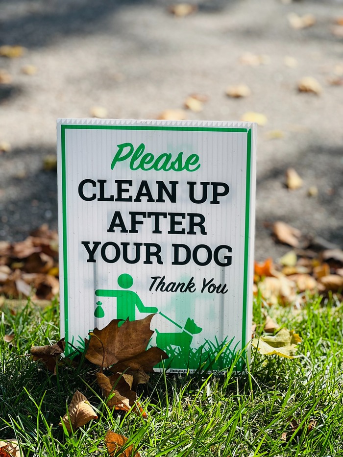Sign on grass reading "Please clean up after your dog," promoting ways to keep dogs from pooping in your yard.
