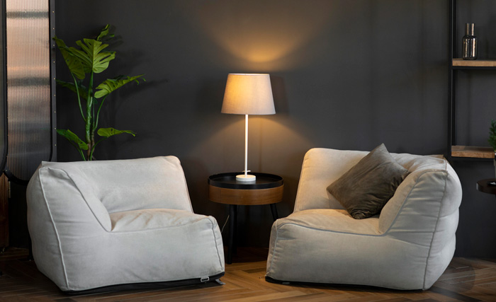 Two white chairs beside a coffee table and warm glowing lamp in a cozy living room with warm colors decor. Two white chairs beside a coffee table and warm glowing lamp in a cozy living room with warm colors decor.