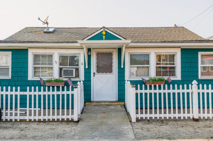 A white wooden fence with spaced-out panels in front of a blue-green house A white wooden fence with spaced-out panels in front of a blue-green house