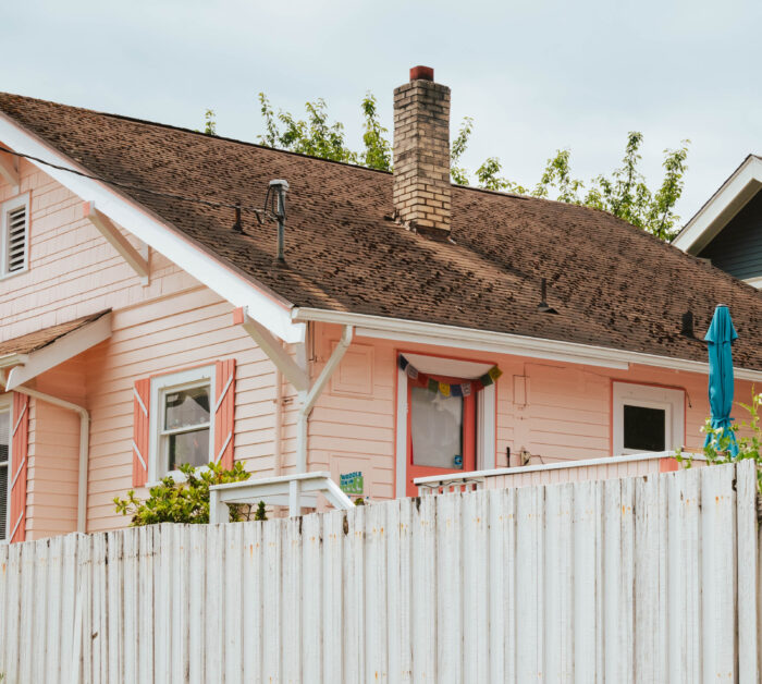 A tall white wooden fence in front of a pink house A tall white wooden fence in front of a pink house