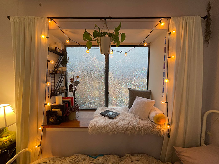 Cozy window seat with fluffy cushions and warm string lights creating a relaxing and inviting space in the home.