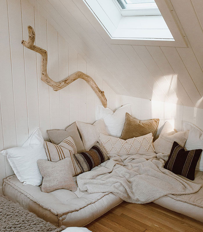 Cozy DIY pillow window seat under skylight in bedroom with neutral cushions and soft blankets for relaxing space.