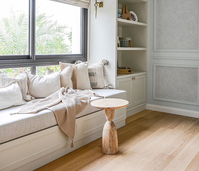 Bright and cozy window seat with soft cushions and a wooden side table in a well-lit modern home space