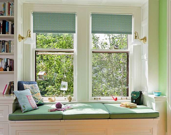 Playful green and white window seat with cushions and pillows beside large windows, creating a cozy space in the home.