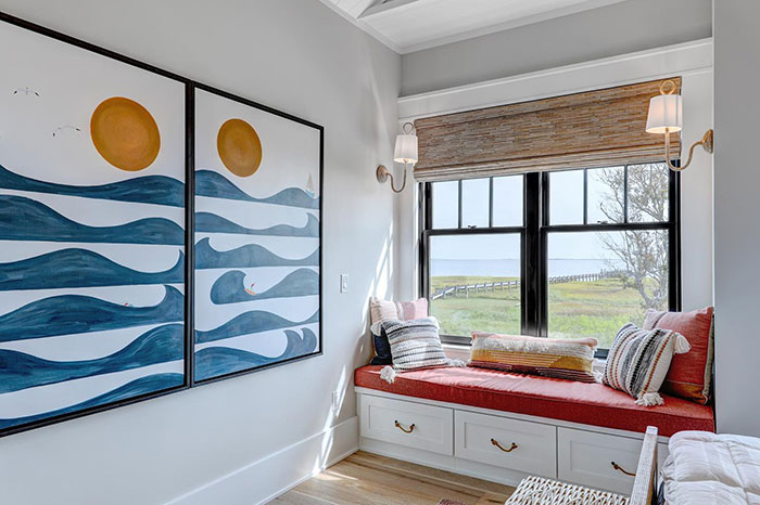 Cozy and minimalist window seat with cushions and storage drawers by a large window overlooking a green landscape.