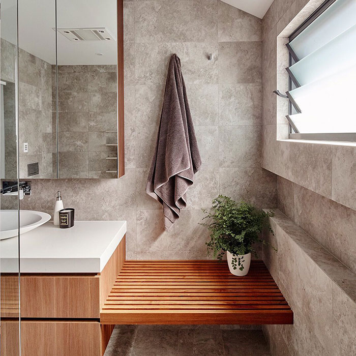 Bright bathroom with a wooden window seat, creating a cozy space with natural light and modern tile design.