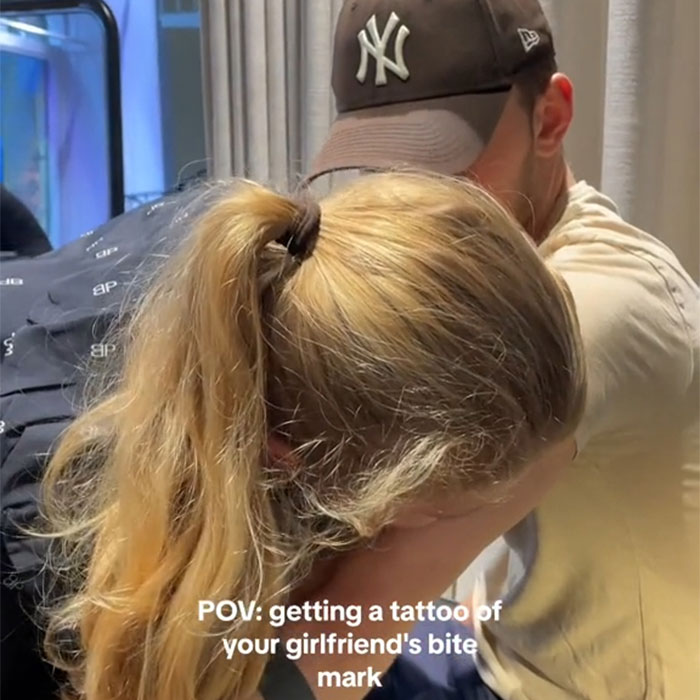 Man with baseball cap gets a tattoo symbolizing love with girlfriend.