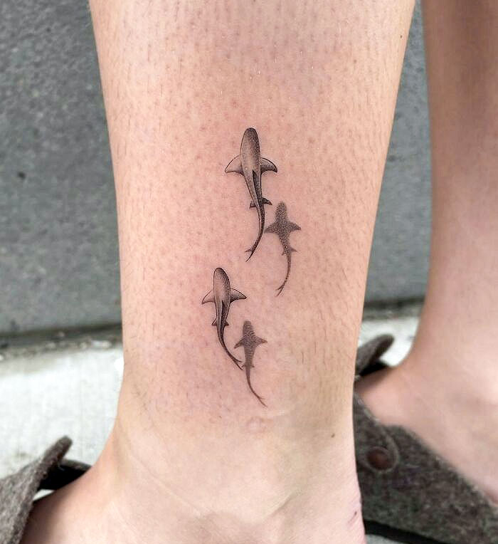 3D shark tattoos on leg, showcasing tattoo artists' skills in creating lifelike designs.