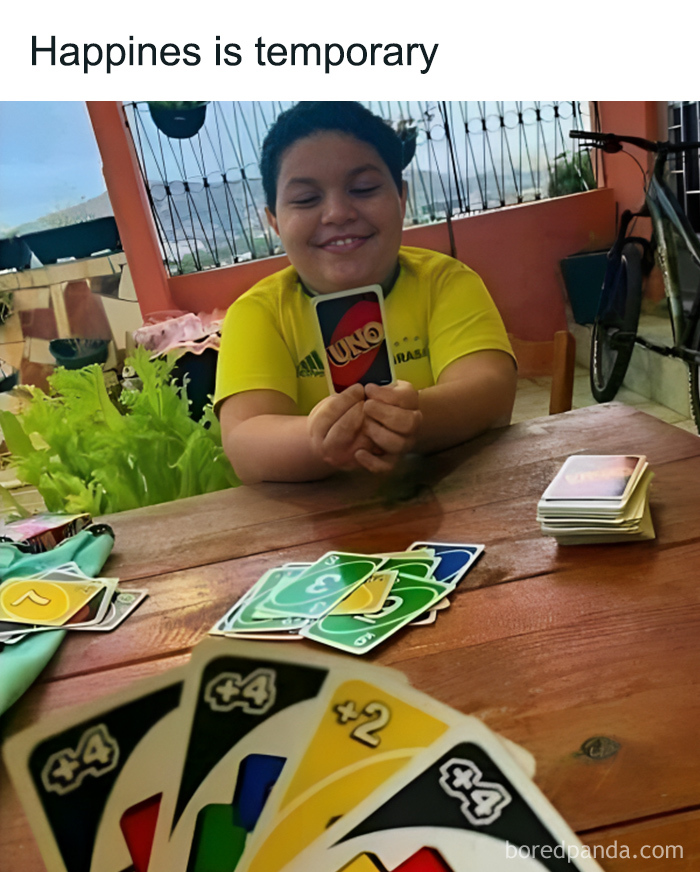 Child smiling while holding an Uno card playing a confusing and unsettling game on a wooden table outdoors.
