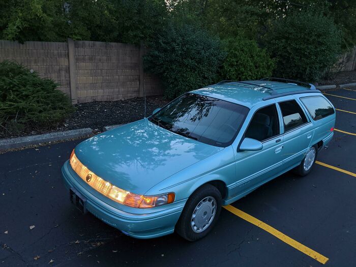 A teal '90s station wagon parked in a lot evokes nostalgia.