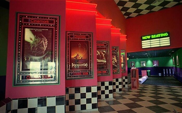 1990s cinema hallway with neon lights, movie posters for Pocahontas and more, evoking nostalgia of classic moviegoing.