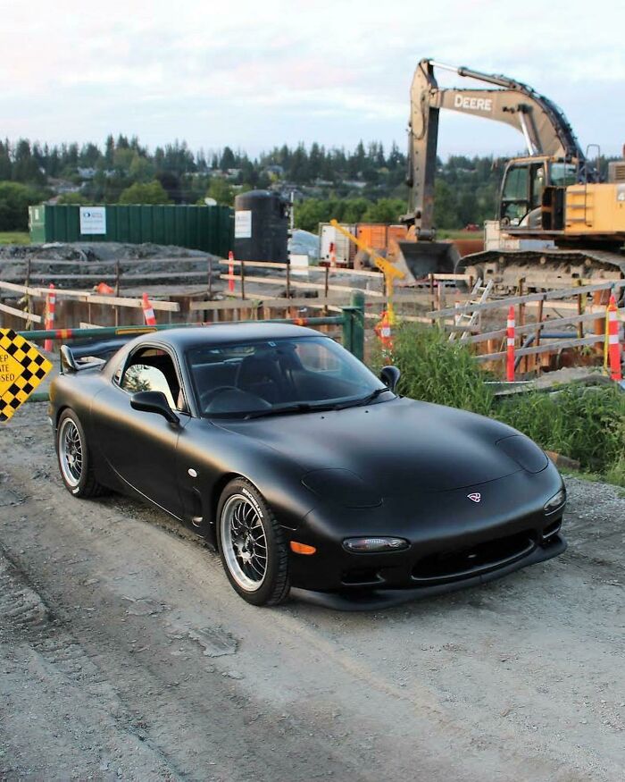 '90s nostalgia: sleek black sports car parked at a construction site, with an excavator in the background.