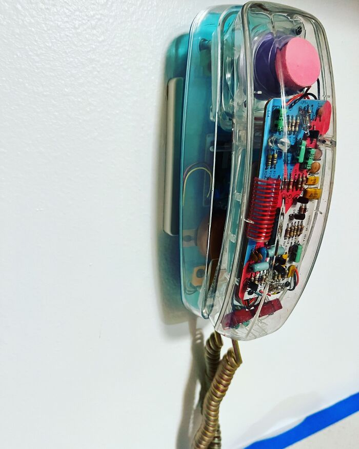 '90s clear landline phone with exposed circuits against a white wall, evoking nostalgia.