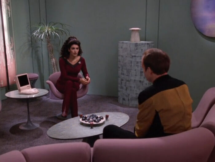 '90s nostalgia scene with two people in futuristic outfits sitting in a retro-style room with vintage tech.