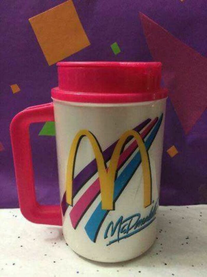 McDonald's vintage '90s mug with colorful stripes and red lid, evoking nostalgia against a geometric patterned background.