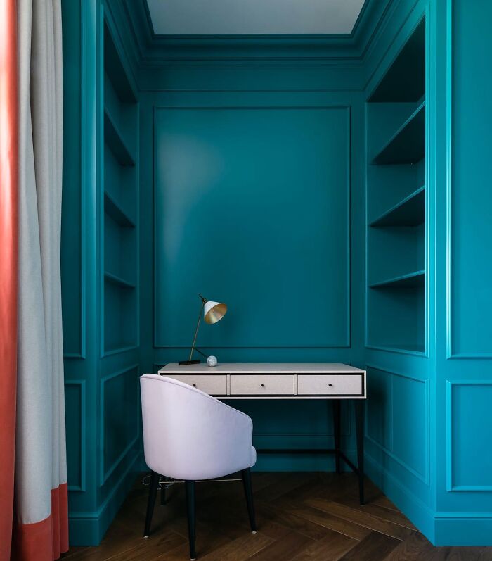 Blue wainscoting panels with built-in shelving surrounding a modern desk and white chair in a cozy home interior.