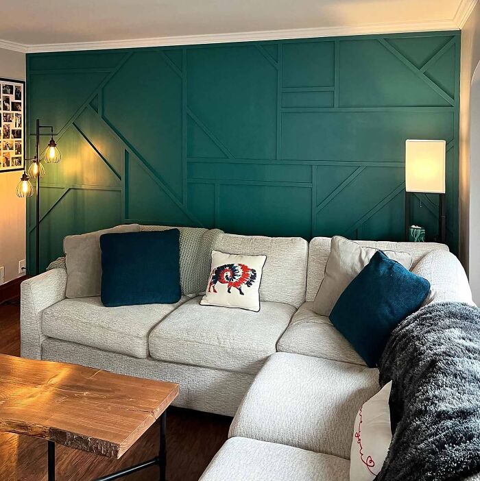 Living room with green geometric accent wall wainscoting, white sectional sofa, decorative pillows, and modern lighting.