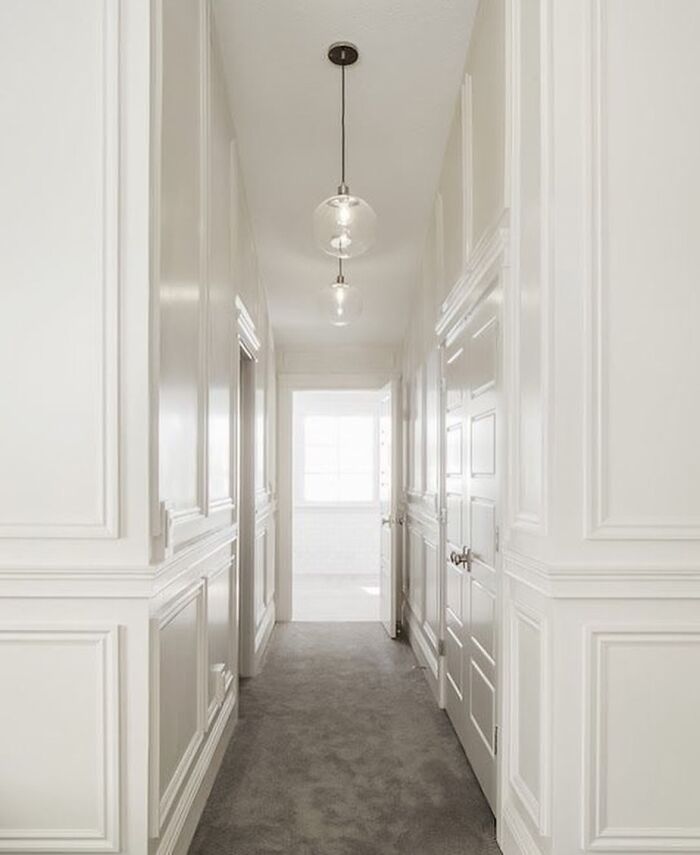 Hallway featuring white high-gloss wainscoting panels and modern pendant lighting in a bright home interior.
