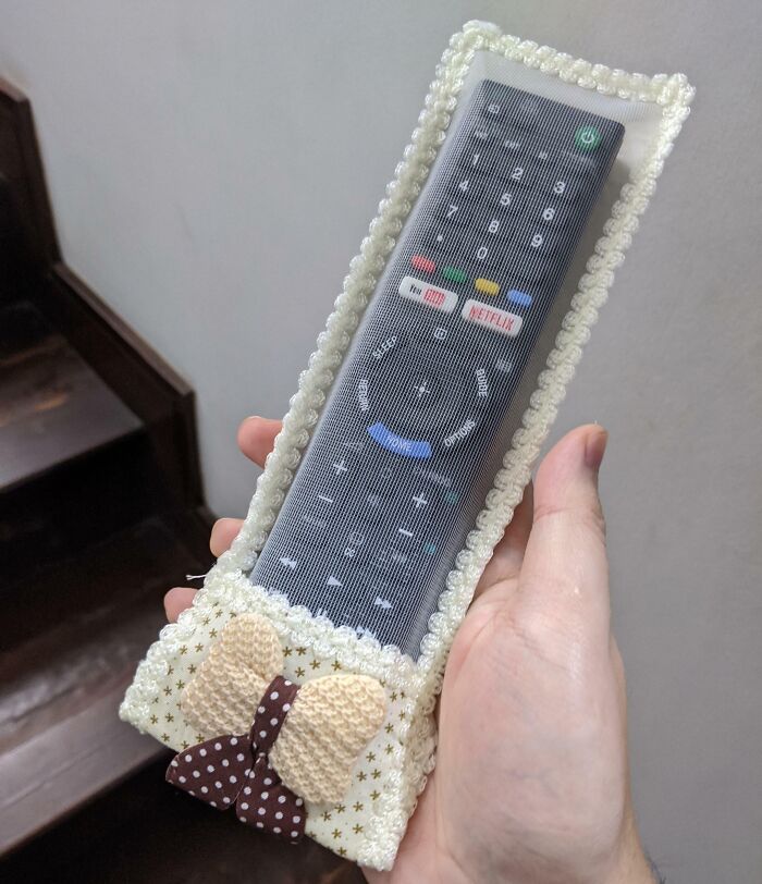 A person holds a TV remote in a crocheted cover with bows, showcasing parents' humor.