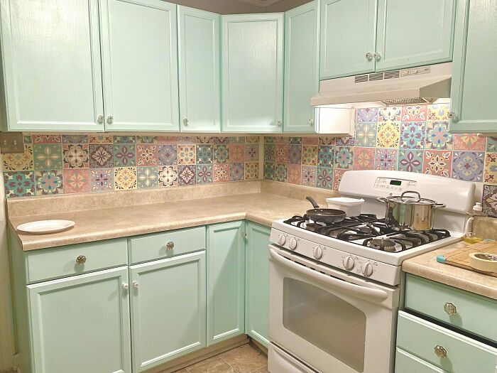 Retro kitchen featuring light green kitchen cabinets with colorful patterned tile backsplash and beige countertops