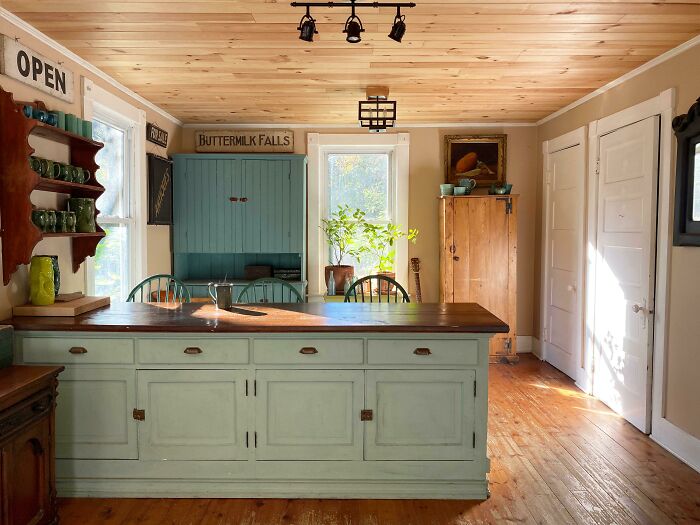 Soft pastel green kitchen cabinets with wooden countertops in a cozy home with natural light and rustic decor.