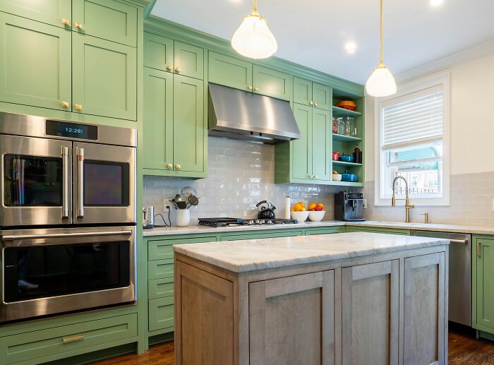 Mint green kitchen featuring green kitchen cabinets, stainless steel appliances, and a marble island countertop.