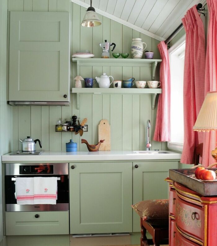 Small kitchen featuring light green kitchen cabinets with open shelving and red gingham curtains by the window